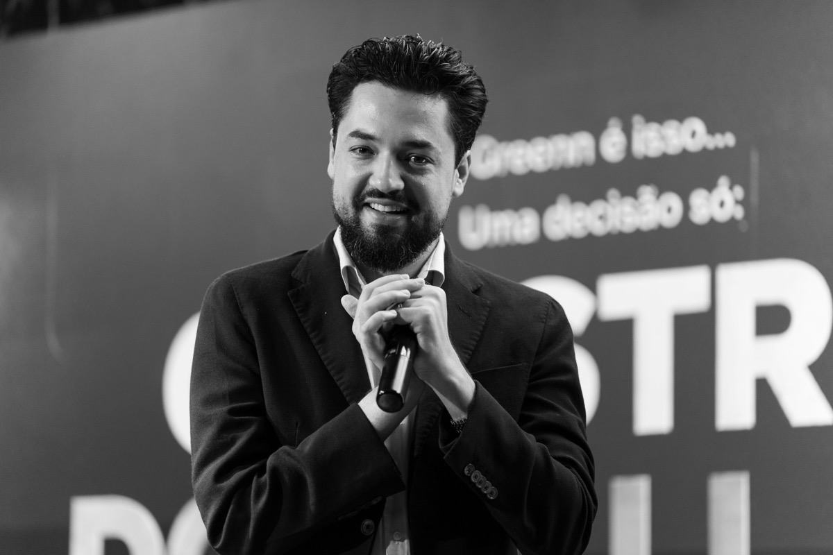 Rafael Wisch no palco, de terno escuro, segurando um microfone e sorrindo